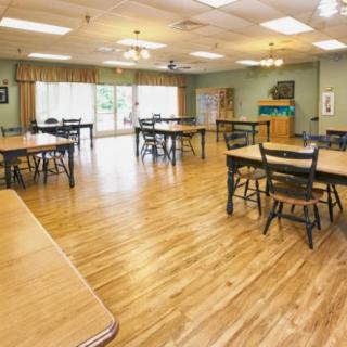 A spacious room with wooden flooring, tables, and chairs arranged neatly.