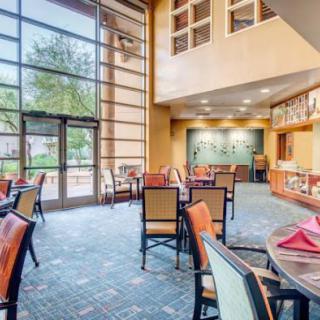 A modern dining area with large windows allowing natural light to illuminate the space, featuring neatly arranged tables and chairs.