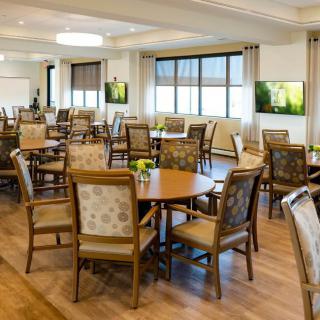 A spacious and modern dining area designed for communal gatherings, featuring wooden tables and upholstered chairs.