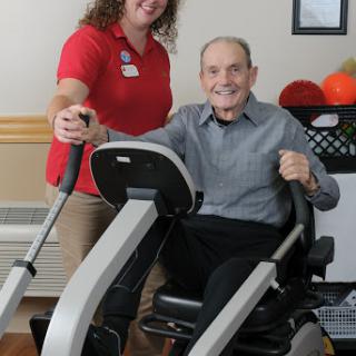 A caregiver assists an elderly man in exercising on a fitness machine, promoting health and rehabilitation.