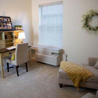 A cozy home office with a desk, chair, and sofa, featuring warm decor and soft lighting.