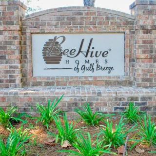 A brick sign for BeeHive Homes surrounded by green plants.