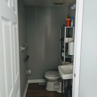 A small, minimalist bathroom with a toilet, sink, and metal shelving unit.