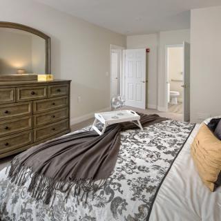 A cozy bedroom with a well-decorated bed, a wooden dresser with a mirror, and neutral color tones.