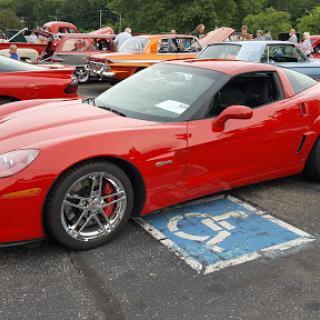 A red Corvette parked over a handicap parking spot at a car show.