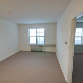 An empty apartment room with a large window and carpeted floor.