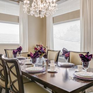 An elegantly set dining table with a chandelier hanging above, featuring purple napkins and tasteful decor.