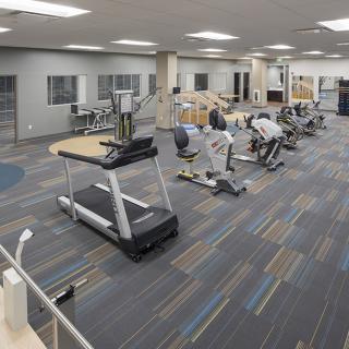 A well-equipped gym with treadmills, stationary bikes, and other exercise equipment on a carpeted floor.