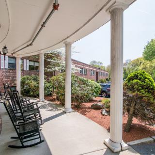 A sunny porch with columns and rocking chairs, surrounded by well-kept landscaping.