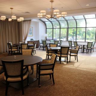A spacious dining area with tables and chairs, featuring large windows that allow natural light to fill the room.