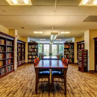 A quiet library room with bookshelves and a central table for reading.