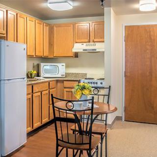 A cozy kitchen and dining area featuring wood cabinets, a refrigerator, microwave, electric stove, and a small table with chairs.