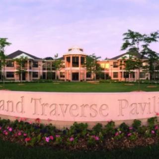 A large, elegant building with a landscaped lawn and a sign in the foreground that says 'Grand Traverse Pavilions'.