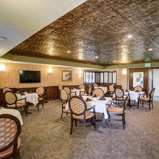 An elegant dining room with neatly arranged tables and chairs, featuring warm lighting and intricate ceiling designs.