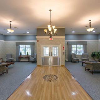A spacious lobby area with a wooden floor, decorative chandelier, and comfortable seating.