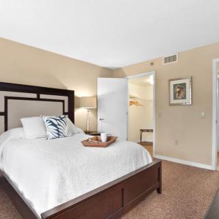 A cozy and minimalist bedroom featuring a large bed with decorative pillows and a bedside lamp.