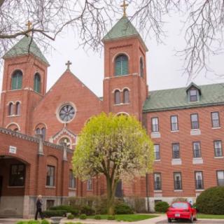 A brick church with twin towers and a green roof, surrounded by trees and a parked red car.