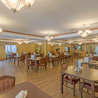 A spacious dining area with multiple tables and chairs, featuring warm lighting and wooden flooring.