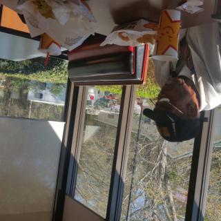 A person sitting at a table in a restaurant with food on the table, next to a window.