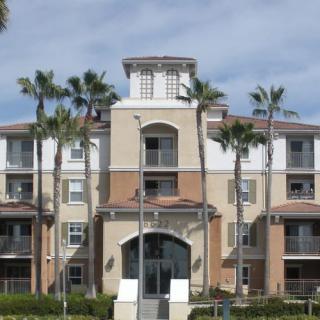 A modern apartment building flanked by palm trees under a blue sky.