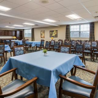A spacious dining room with neatly arranged tables and chairs, featuring blue tablecloths and simple decor.