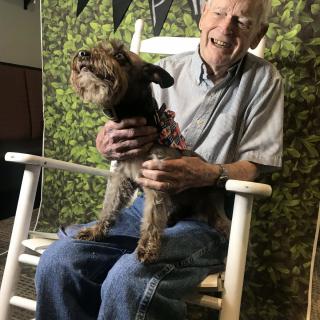 An elderly man sitting in a rocking chair with a dog on his lap, both looking content.