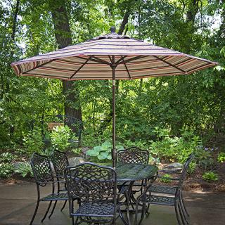 A scenic outdoor patio area featuring a table with chairs and a large umbrella, surrounded by lush greenery.