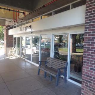 Exterior view of a restaurant with glass windows and a wooden bench outside.