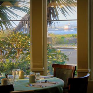 A peaceful restaurant dining area with a view of the ocean and palm trees through large windows.