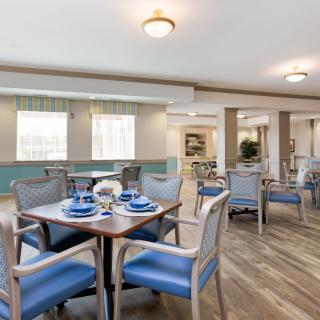 A well-lit dining area featuring blue-upholstered chairs and wooden tables on a wood floor.