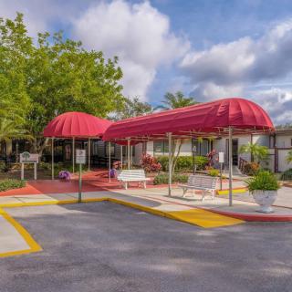 Building entrance with a red canopy and landscaped surroundings on a cloudy day.