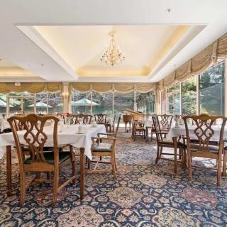 A spacious and elegant dining area with large windows allowing natural light to fill the room, featuring a chandelier and classic wooden furniture.