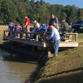 A group of people enjoying a day of fishing off a wooden pier by the lake.