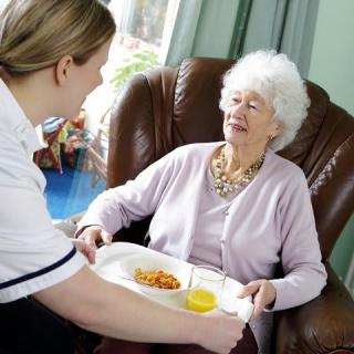 A caregiver serving a meal to an elderly woman in a comfortable chair.