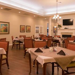 A cozy and elegant dining area with neatly arranged tables and chairs, featuring a fireplace and chandelier.