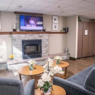 A cozy lobby area with comfortable seating, a central fireplace, and a television mounted above, decorated with flowers on coffee tables.