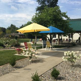A vibrant outdoor patio featuring yellow and blue umbrellas, surrounded by lush landscaping and flowers.
