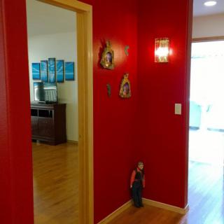 A warmly decorated hallway with a vibrant red wall and wooden flooring, leading to a room with natural light.