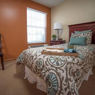 A cozy bedroom with a single bed, featuring a decorative bedspread and pillows, next to an orange accent wall.