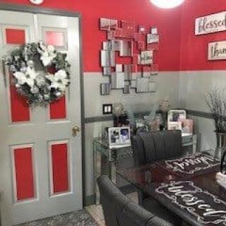 A cozy dining area with red and gray decor, featuring a wreath on the door and framed pictures.