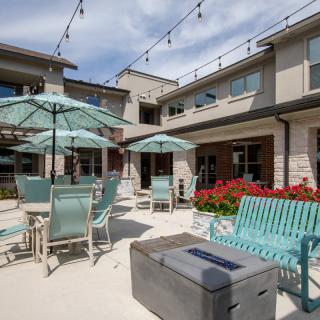 A sunny outdoor patio with seating and umbrellas, surrounded by a modern building.