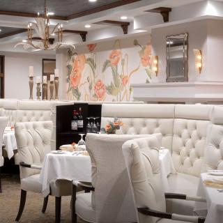 An elegantly decorated restaurant with white upholstered seating and chandeliers, featuring a sophisticated dining atmosphere.