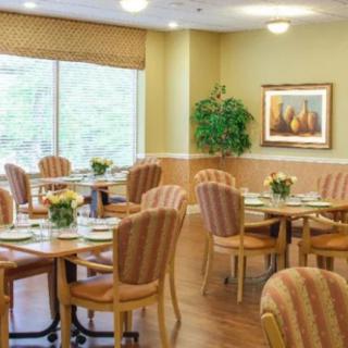 A well-lit dining area with neatly arranged tables and chairs, featuring decorative plants and artwork.