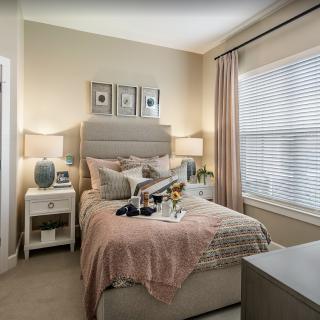 A cozy bedroom with a neatly made bed, side tables with lamps, and large windows covered by curtains.