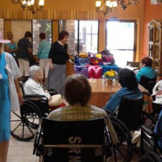 A group of elderly individuals in wheelchairs gathered in a community room within a nursing home.