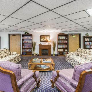 A cozy living room with patterned sofas, armchairs, bookshelves, and a fireplace.