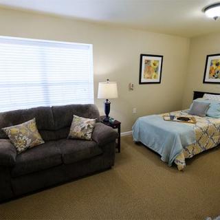 A cozy bedroom with a sofa and bed, decorated with artwork and illuminated by a lamp.