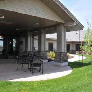 A covered patio with outdoor seating surrounded by a well-maintained lawn and modern building architecture.