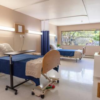 A hospital room with two beds, medical equipment, and a large window offering natural light.