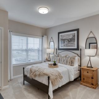 A cozy bedroom with neutral tones, featuring a neatly made bed, side tables with lamps, and a large window allowing natural light.